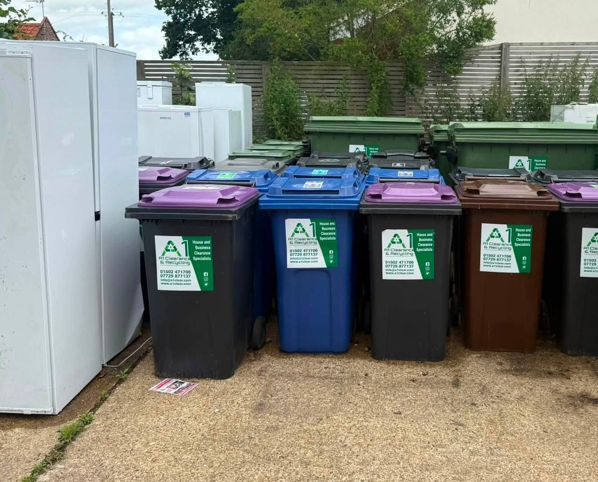 Colour coded A1 Clearance and Recycling wheelie bins lined up beside stacked fridges at the company yard for sorting and recycling